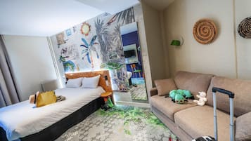 A hotel room with a bed, a sofa, a suitcase, and a mirror reflecting the room.