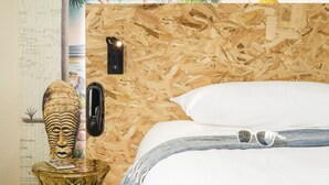 Une pièce avec un mur en bois, un lit recouvert de draps blancs, une petite table ornée d’un objet décoratif et un luminaire fixé au mur.