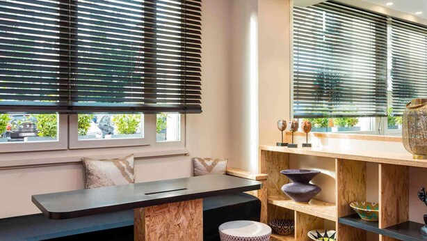 Un intérieur moderne avec un banc, une étagère en bois agrémentée d’objets décoratifs et une grande fenêtre avec des stores.