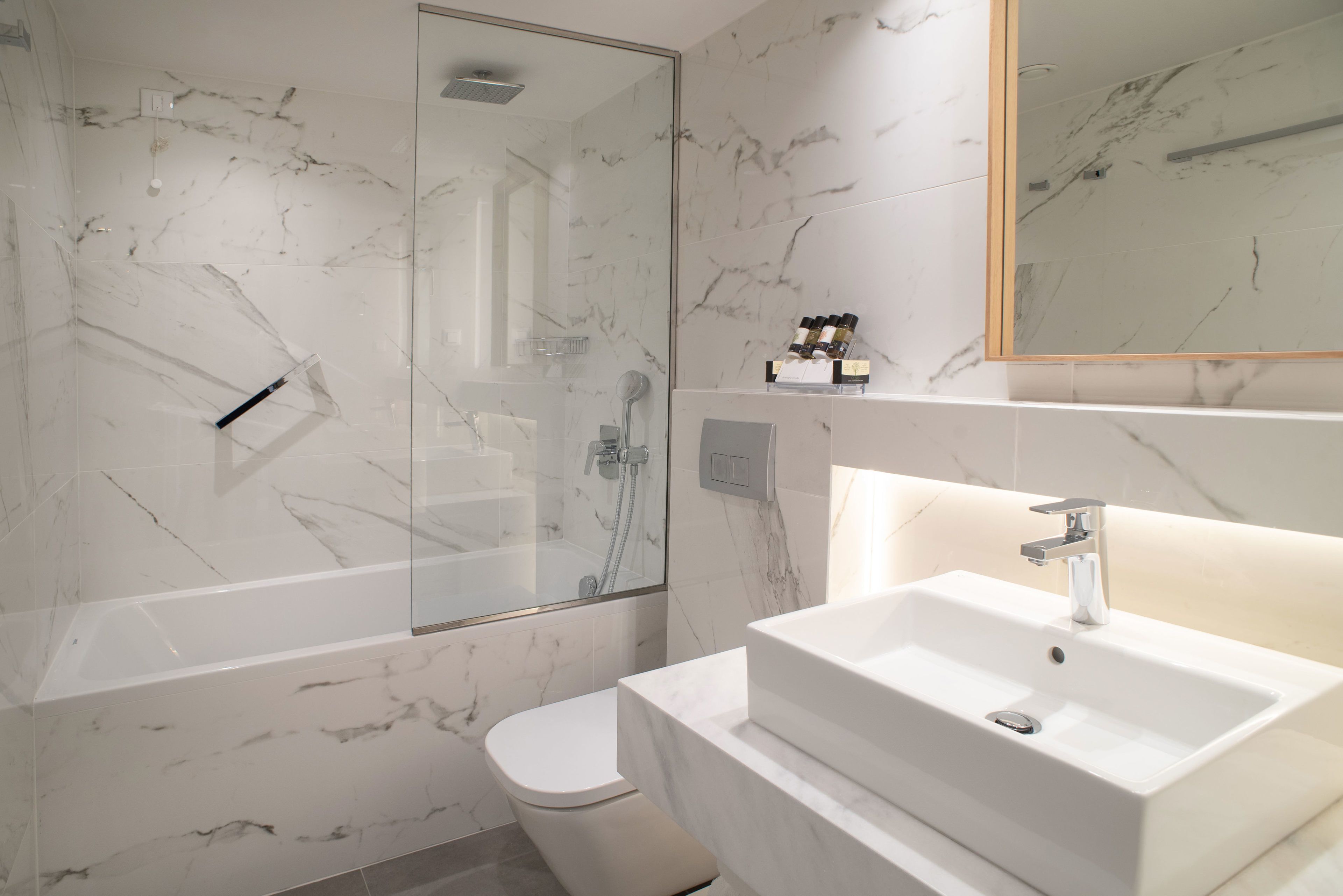 Et moderne badeværelse med et brusebad i glasboks, en hvid vask og et toilet.