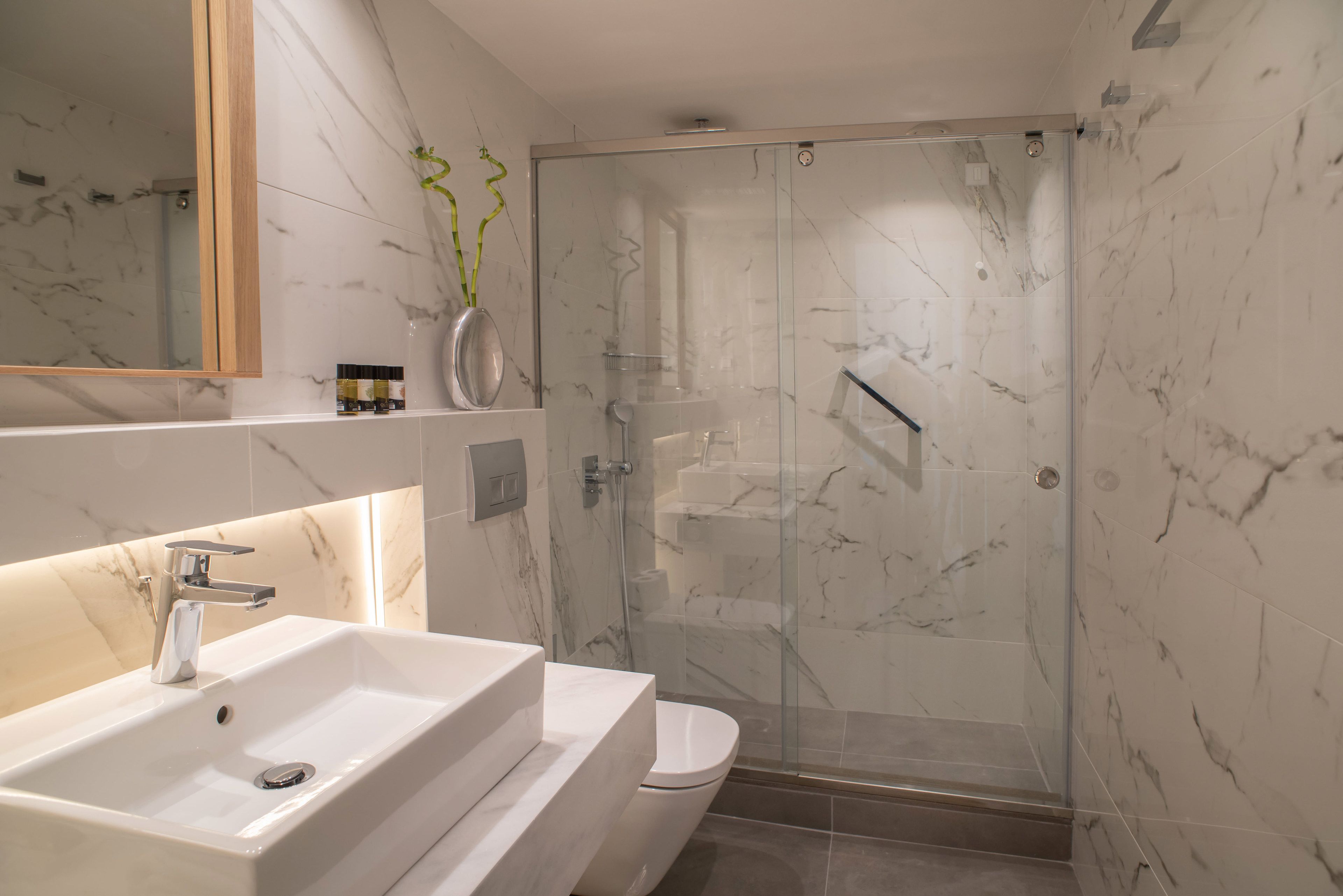 A modern bathroom with a white sink, mirror, and glass shower enclosure.