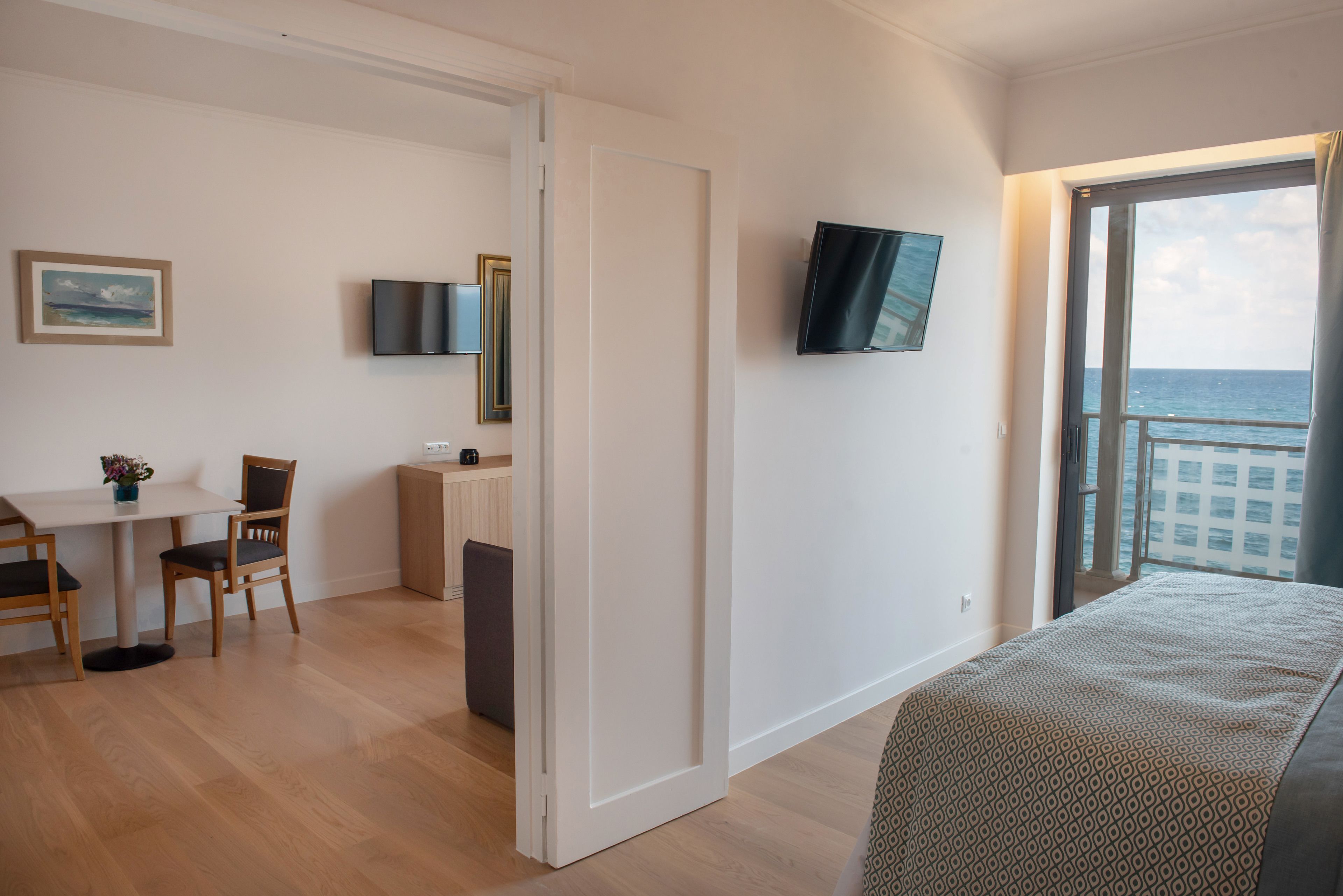 Une chambre d’hôtel avec un lit, un bureau et une chaise, un téléviseur fixé au mur et une vue sur la mer par une grande fenêtre.