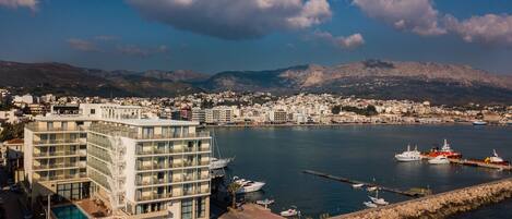 A coastal cityscape with a marina, buildings, and mountains in the background.