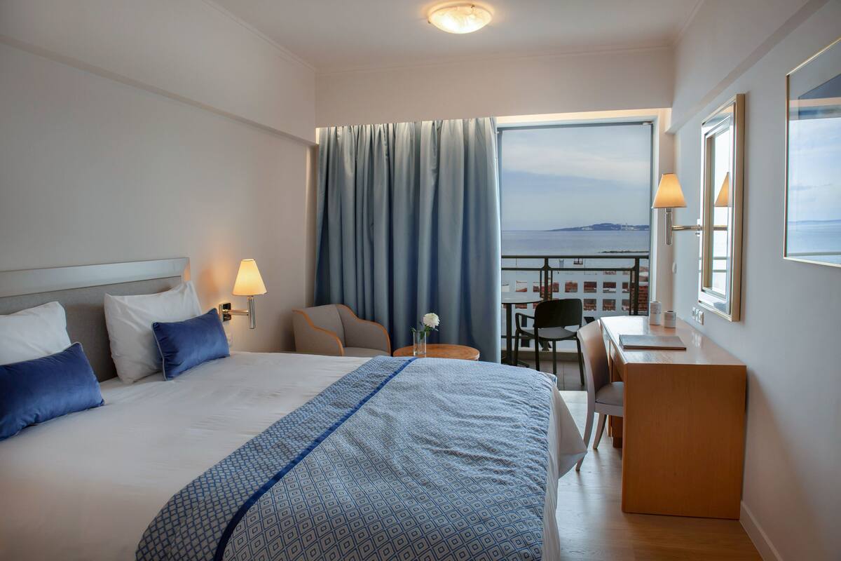 A hotel room with a bed, a desk, and a view of the sea.