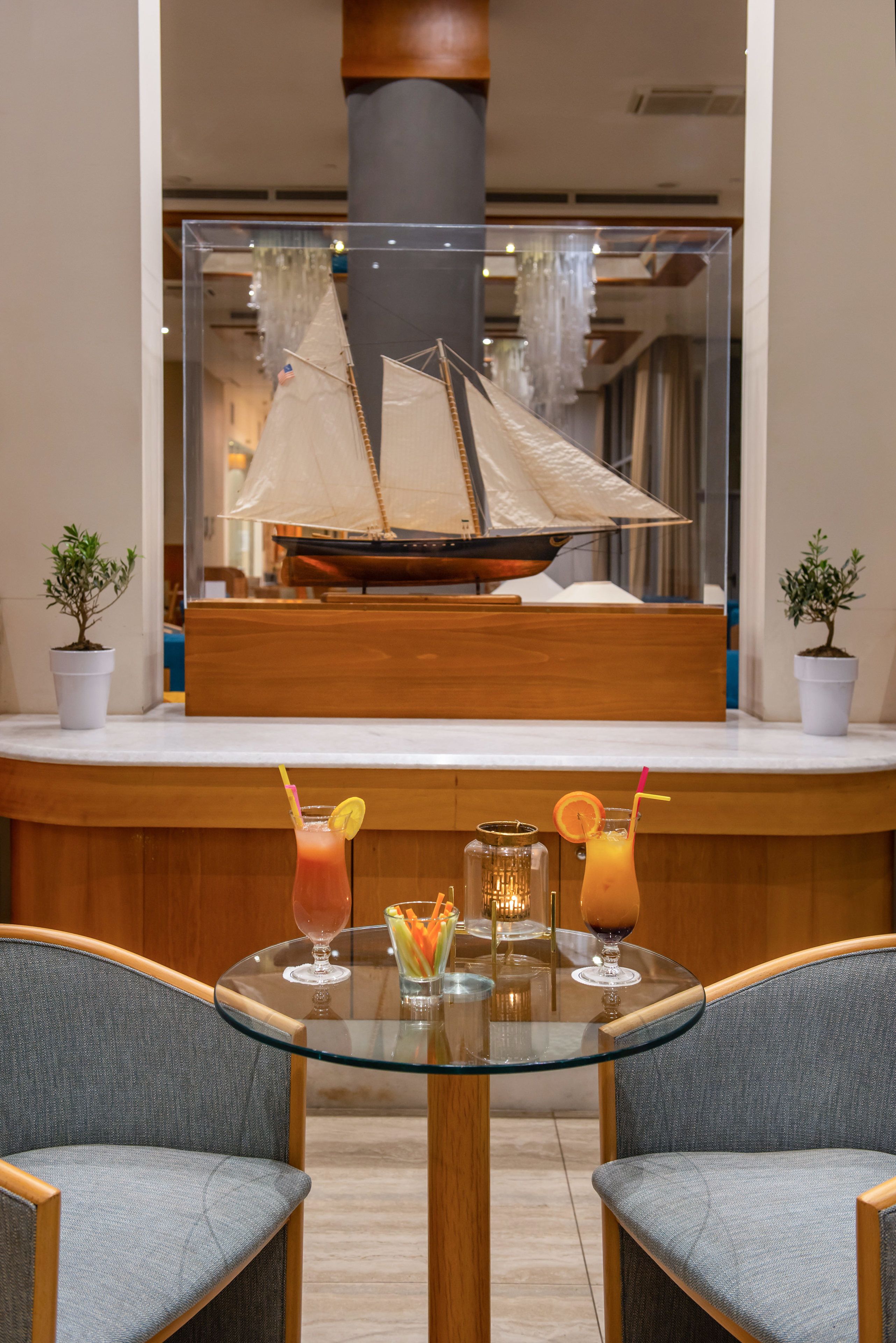 A hotel lobby with a glass table, two chairs, and a large mirror reflecting a sailboat model.