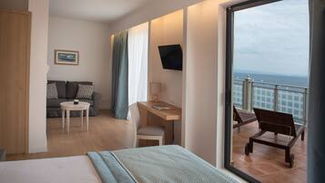 Habitación de hotel con cama, escritorio, silla, sofá y balcón con vistas al mar.