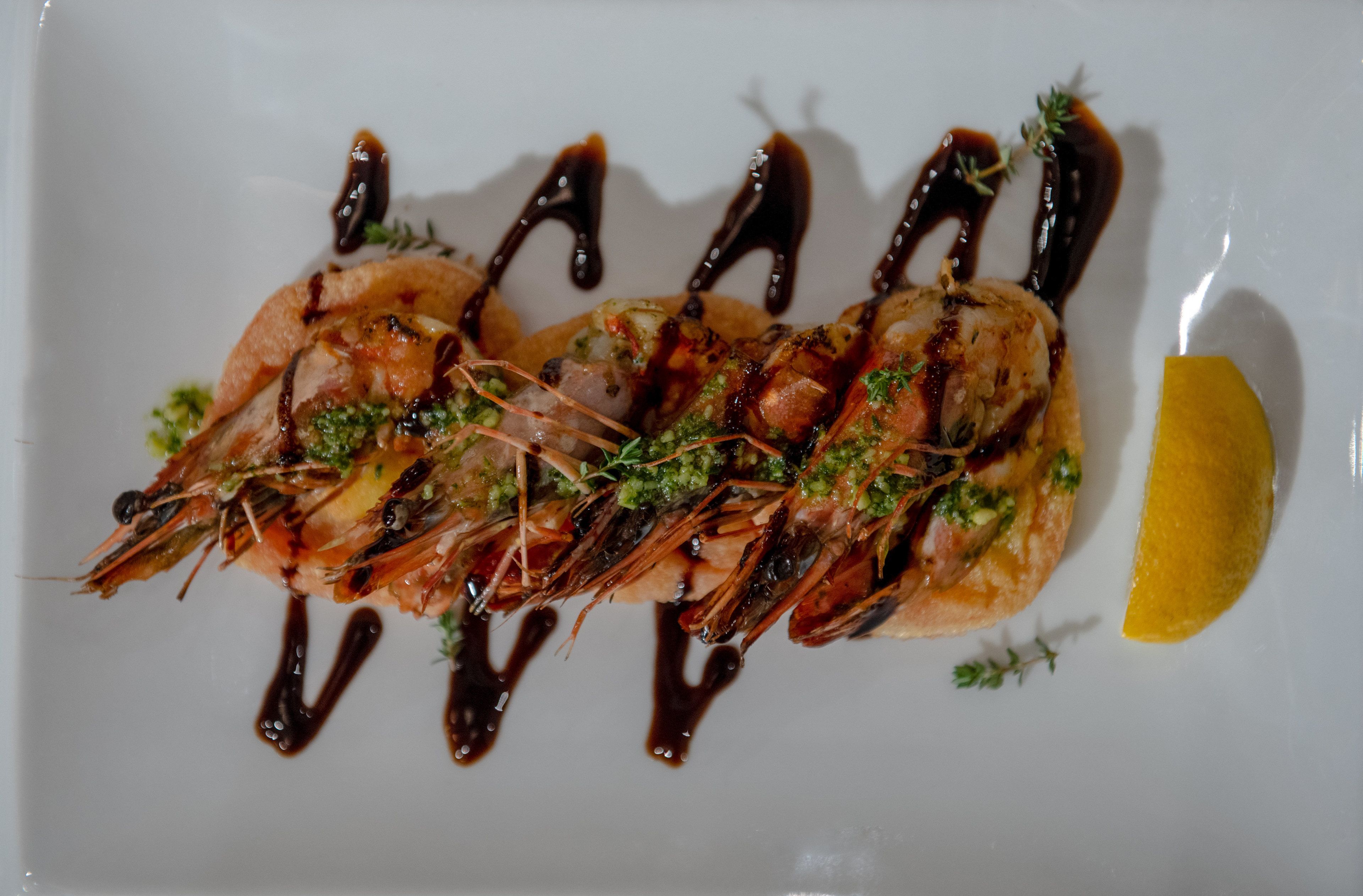 A plate of grilled shrimp with sauce and garnish.
