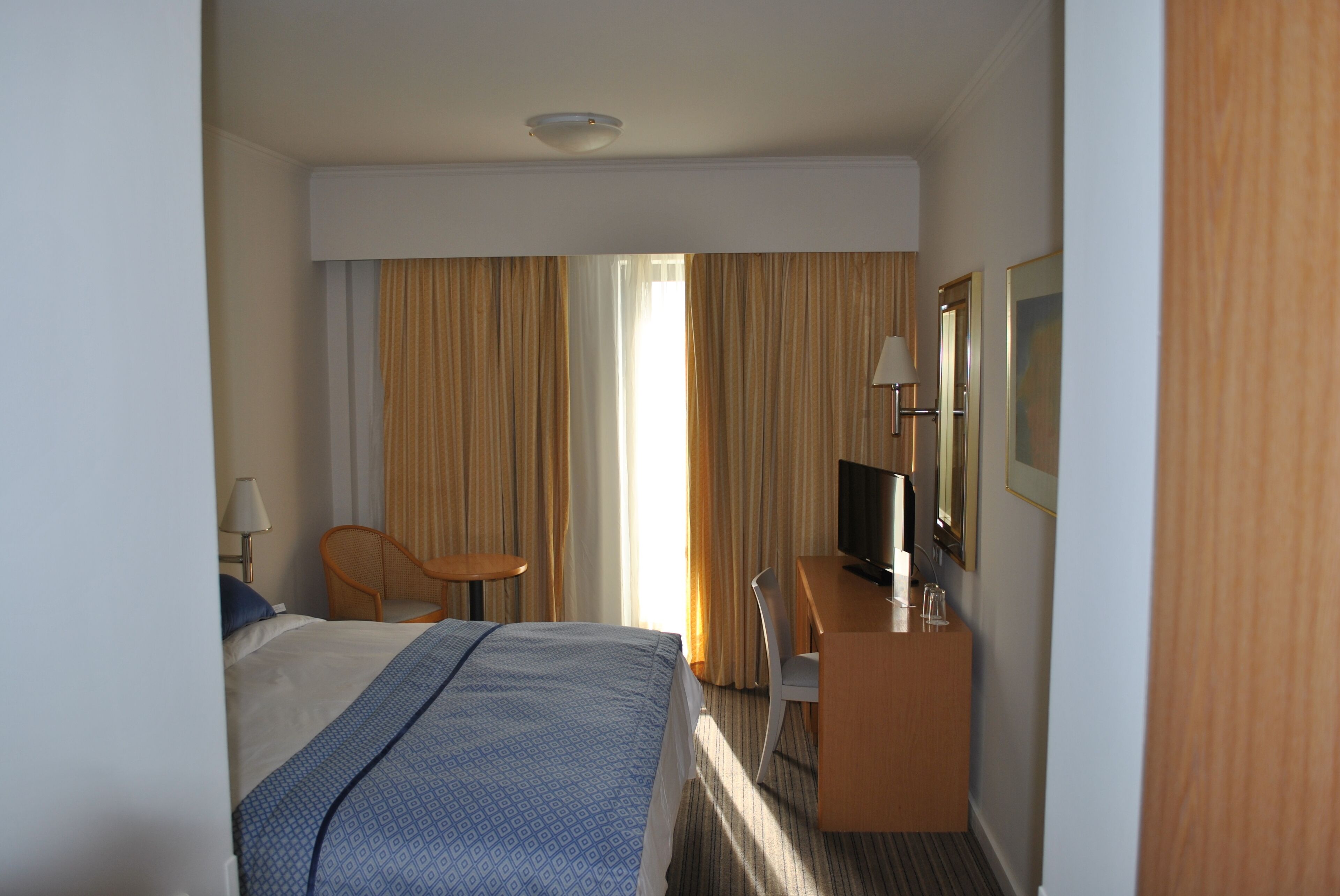 A hotel room with a bed, a desk, a chair, a television, and a mirror.