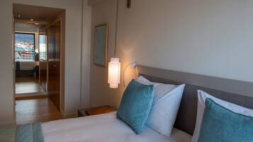 Una camera d'hotel con un letto, un comodino, una lampada e vista sulla città attraverso un'ampia finestra.