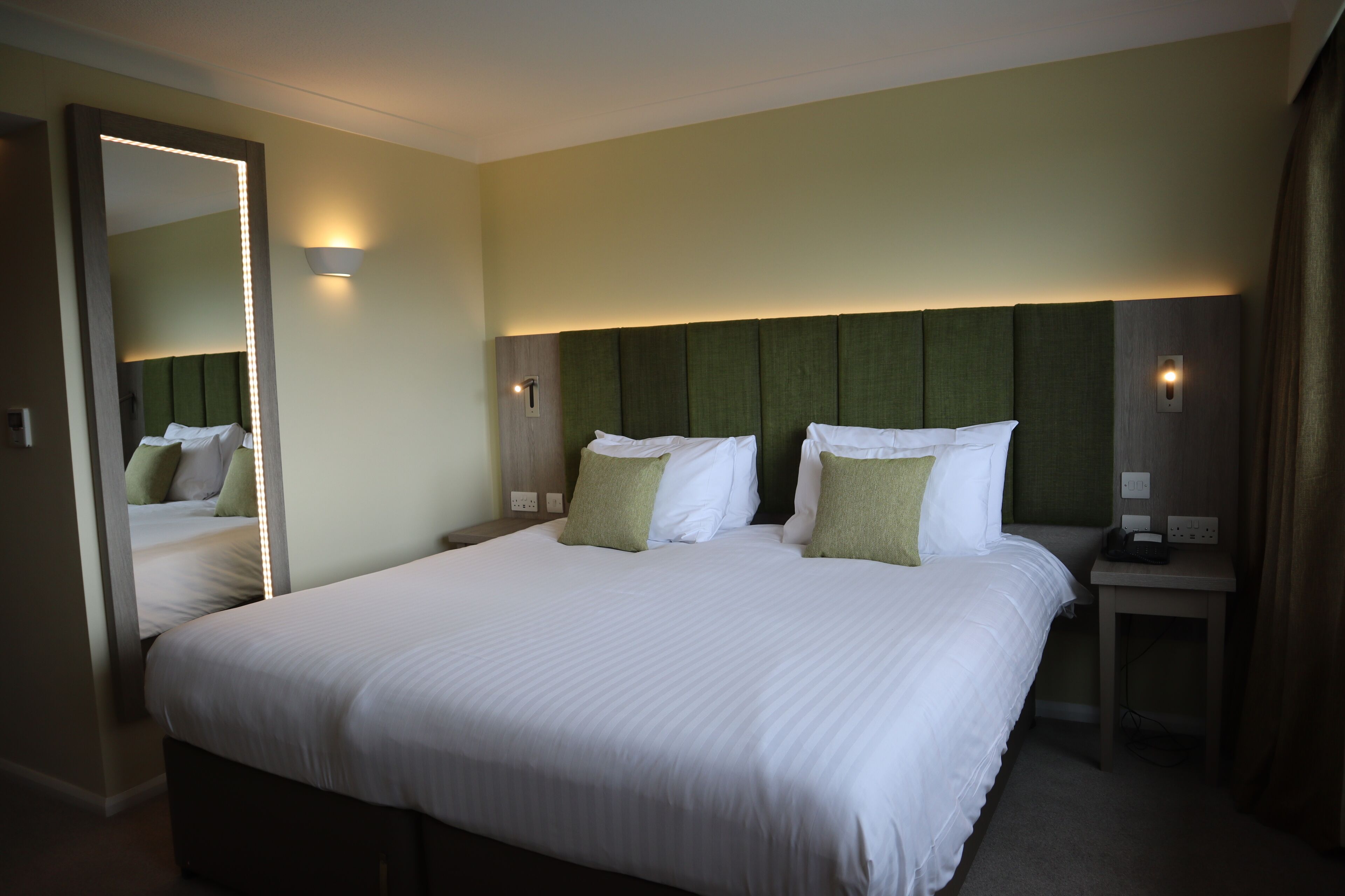 Una habitación de hotel con una cama grande, un espejo, lámparas de noche y una mesita de noche.