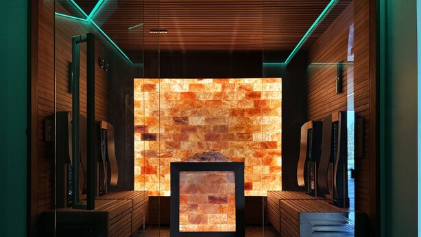 A modern interior with a stone wall, wooden paneling, and a central fireplace. - Hellidon Lakes Golf & Spa Hotel (Daventry)
