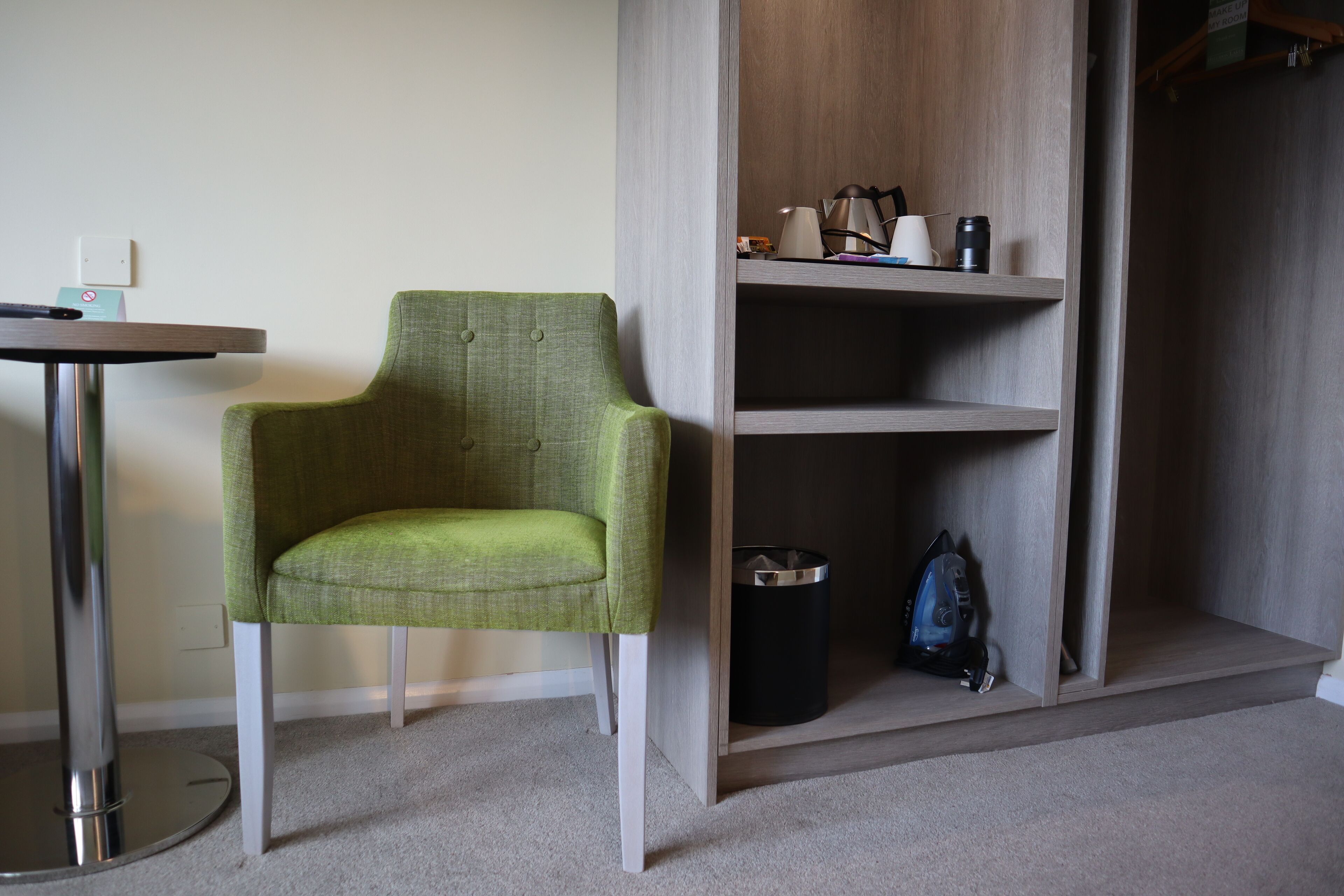 Una habitación con un sillón verde, una mesita pequeña y una estantería de madera con varios objetos.