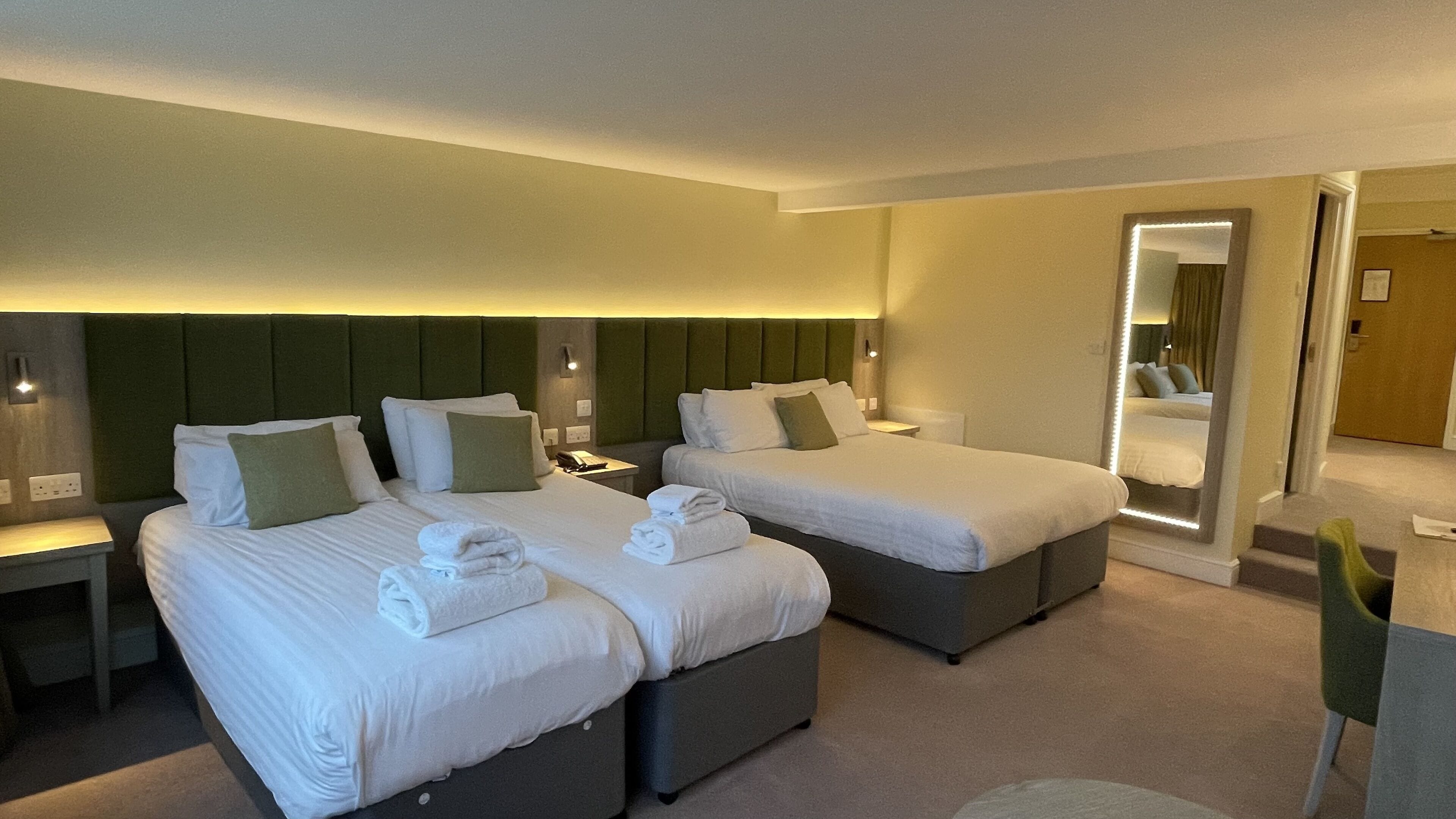 A hotel room with two beds, each with a headboard, bedside tables, and a mirror.
