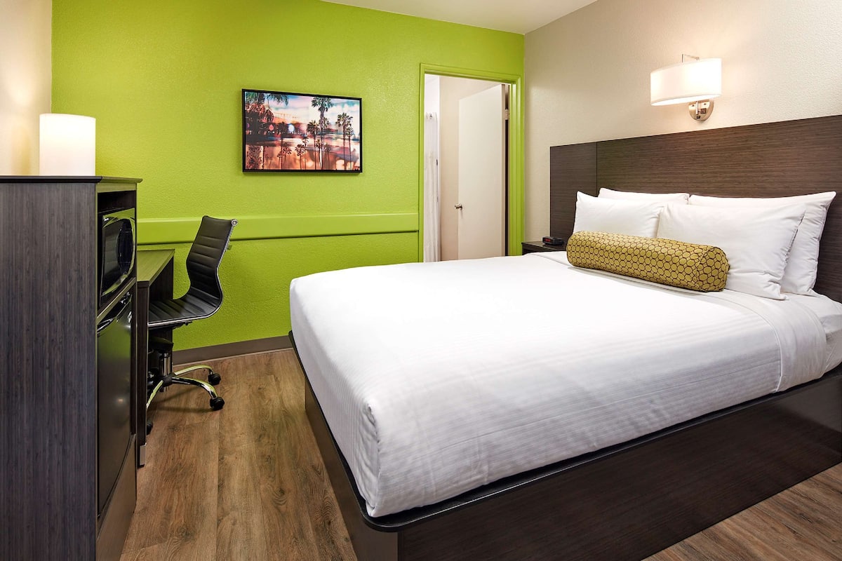 Ein Hotelzimmer mit Bett, Schreibtisch, Stuhl, einem Bild an der Wand und einer Tür.