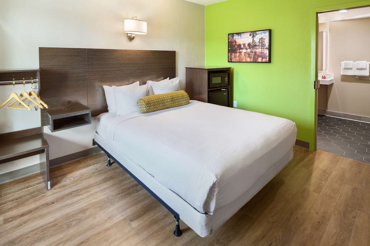 Ein Hotelzimmer mit Bett, Nachttisch, Fernseher, Mikrowelle und einer grünen Wand.