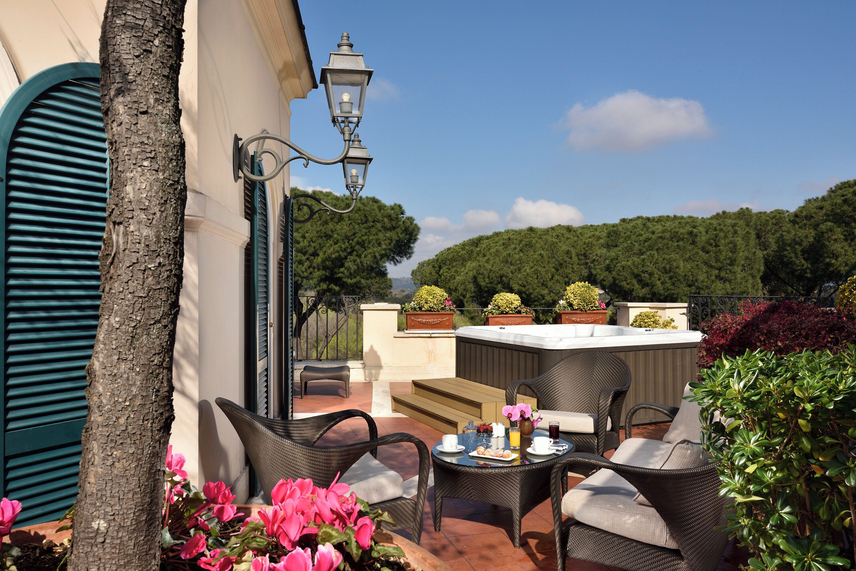Un patio al aire libre con mobiliario de mimbre, una mesa con un florero y una taza, y vistas a una colina verde.