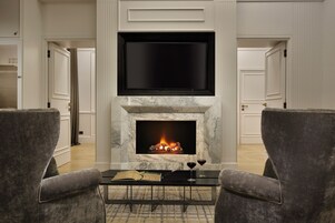A living room with a fireplace, a flat-screen TV, two armchairs, and a coffee table.