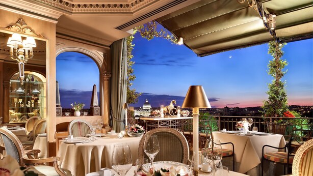 Une salle à manger luxueuse, agrémentée de lustres somptueux, d’une décoration de table élégante et offrant une vue imprenable sur le paysage urbain au crépuscule.