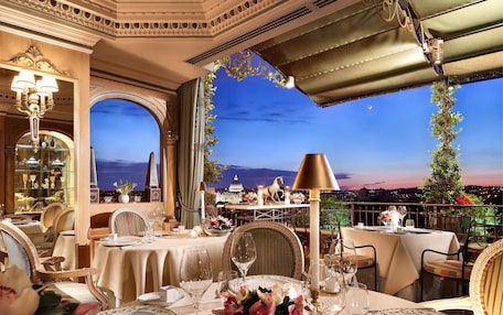 A luxurious dining area with ornate chandeliers, elegant table settings, and a scenic view of the cityscape at dusk.