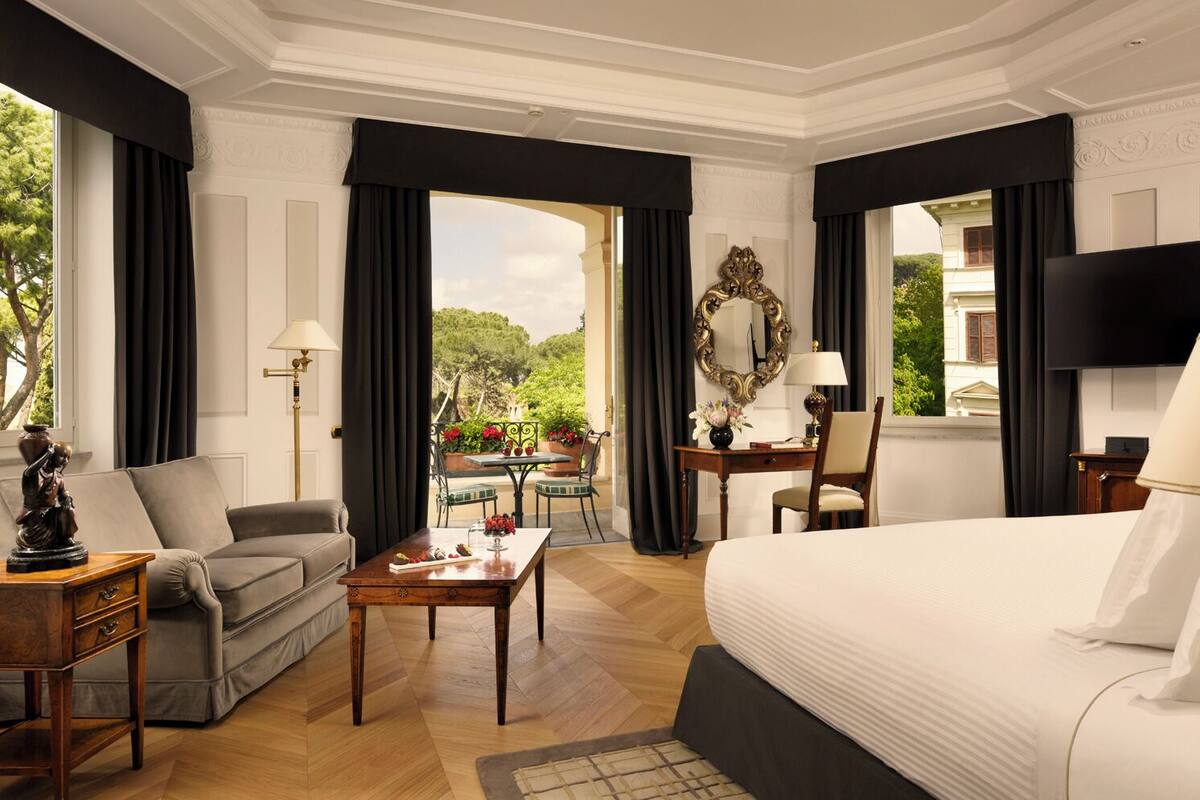 Ein Hotelzimmer mit Bett, Sofa, Schreibtisch und Esstisch. Ein Fenster bietet Blick auf Grünfläche.