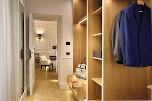 A modern hotel room with a wooden wardrobe, a dining area, and a hallway leading to a kitchen.