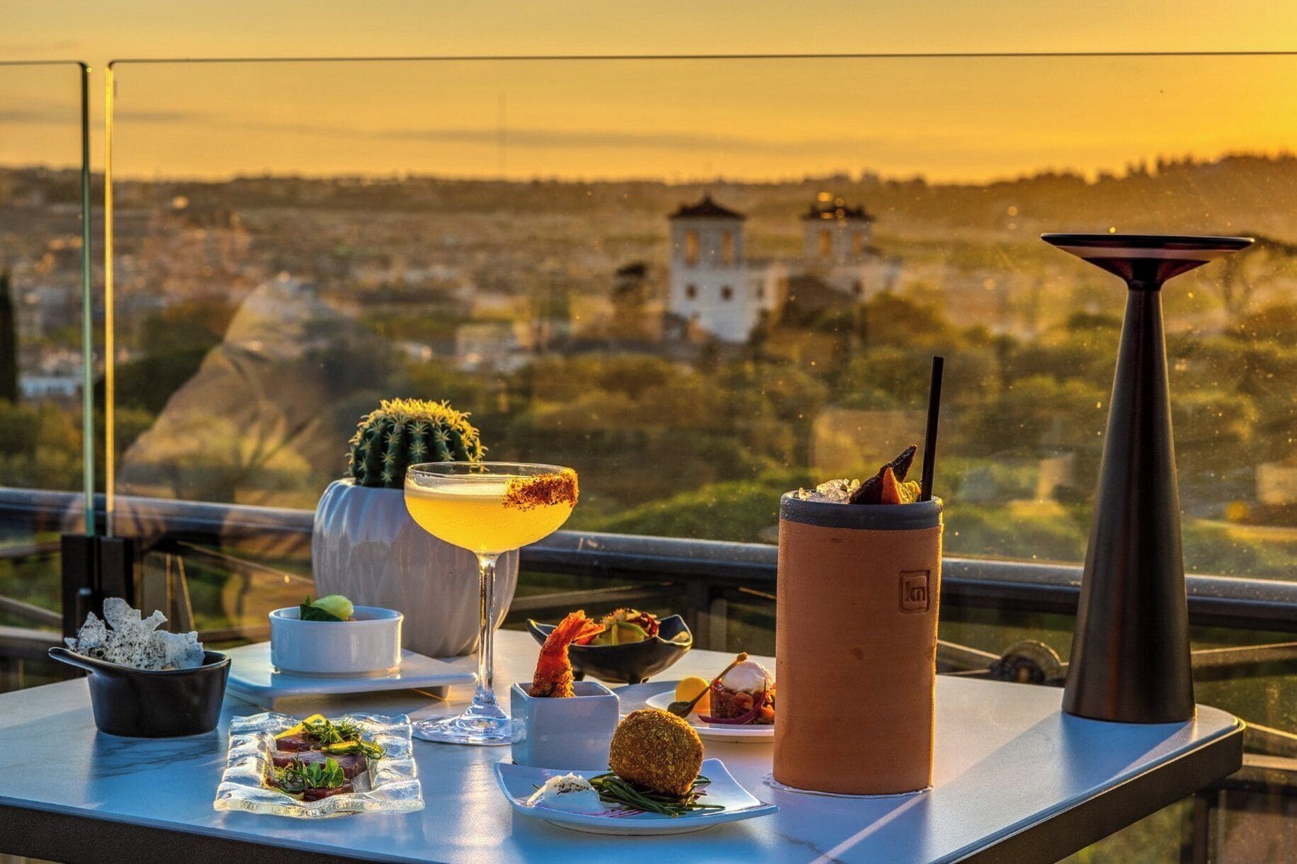 Une table avec des boissons, de la nourriture et une vue sur le paysage urbain.