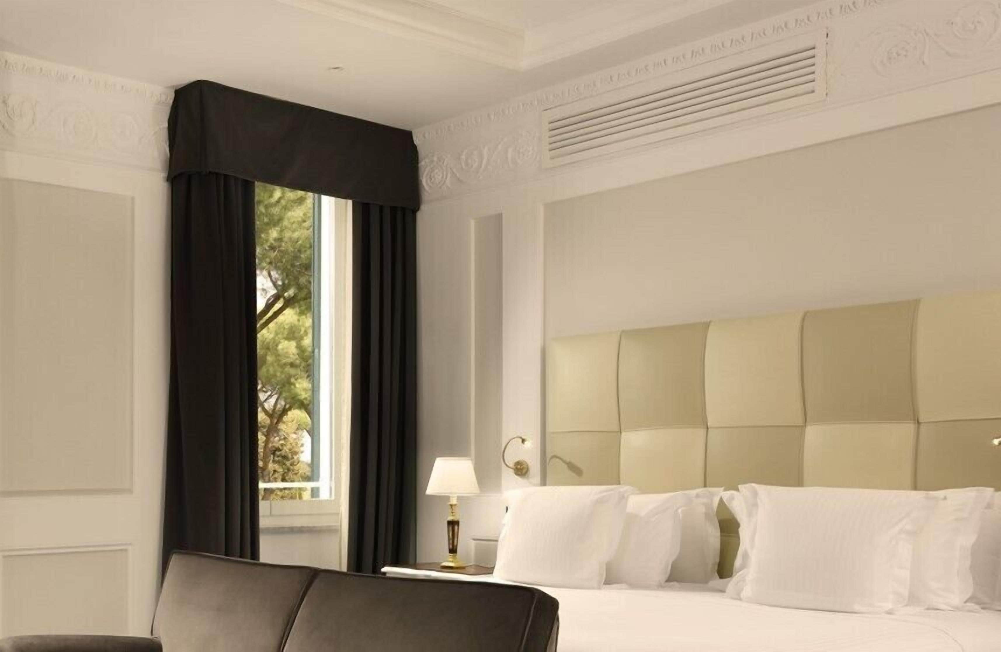 Una habitación de hotel con una cama grande, una mesita de noche con lámpara y una ventana con cortinas.