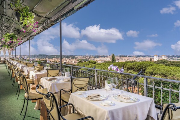 A terrace with tables set for dining, overlooking a cityscape with historical buildings.