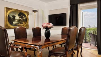 A conference room with a wooden table, leather chairs, a vase with flowers, a painting, and a TV on the wall.
