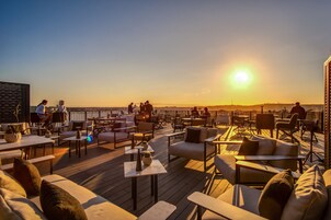 A rooftop terrace with outdoor seating, tables, and a view of the sunset.