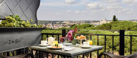 A balcony with wicker chairs, a table set with breakfast, and a view of a cityscape including a prominent dome building.