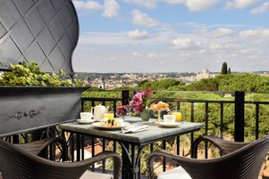 Un balcone con sedie in vimini, un tavolo apparecchiato per la colazione e vista su un paesaggio urbano che include un edificio a cupola ben visibile.