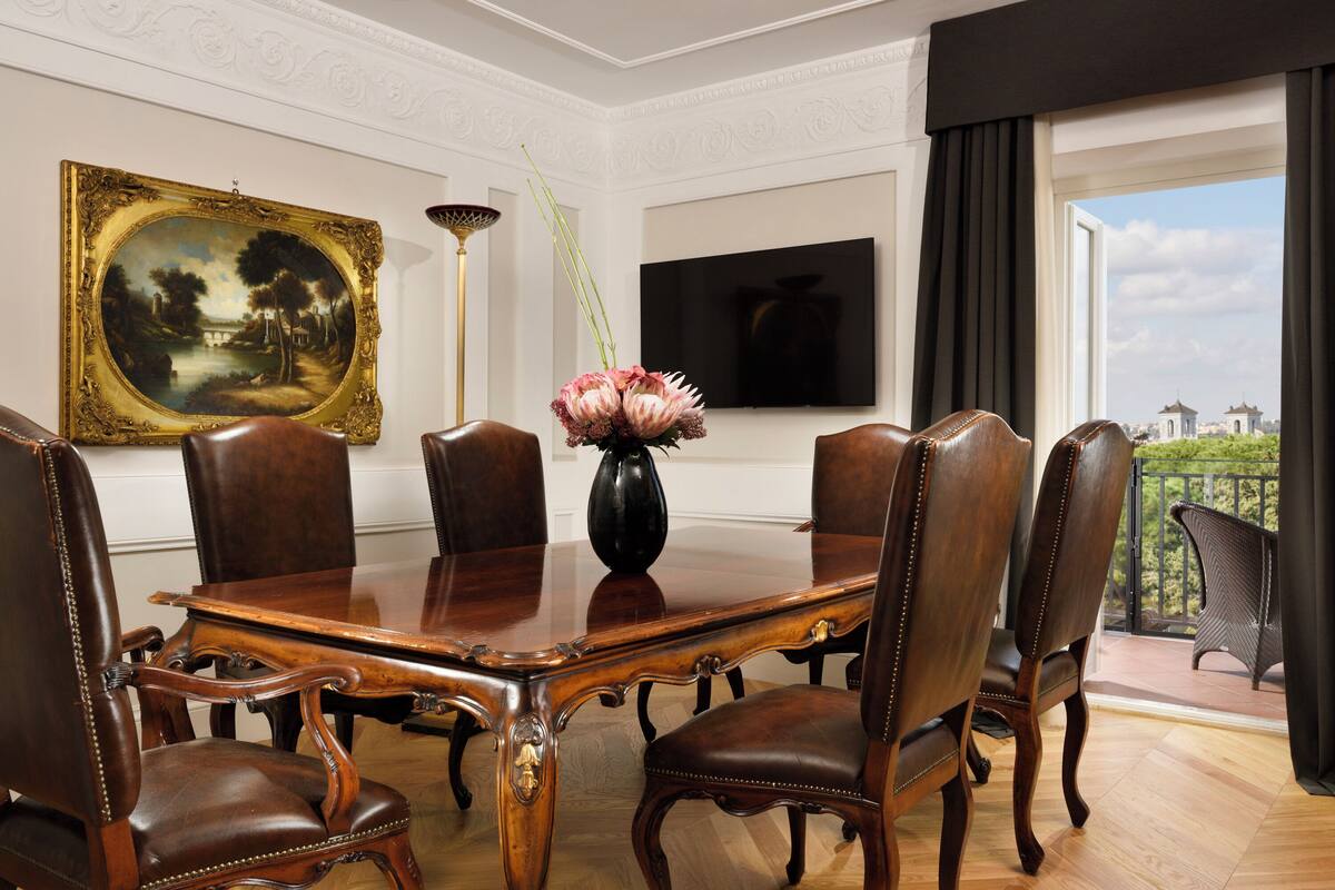 Ein Konferenzraum mit Holztisch, Ledersesseln, einer Vase mit Blumen, einem Gemälde und einem Fernseher an der Wand.
