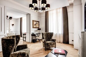 Egy tágas nappali, melyben egy nagyméretű csillár függ, egy étkező fehér asztallal és székekkel, és a háttérben egy modern konyha található.