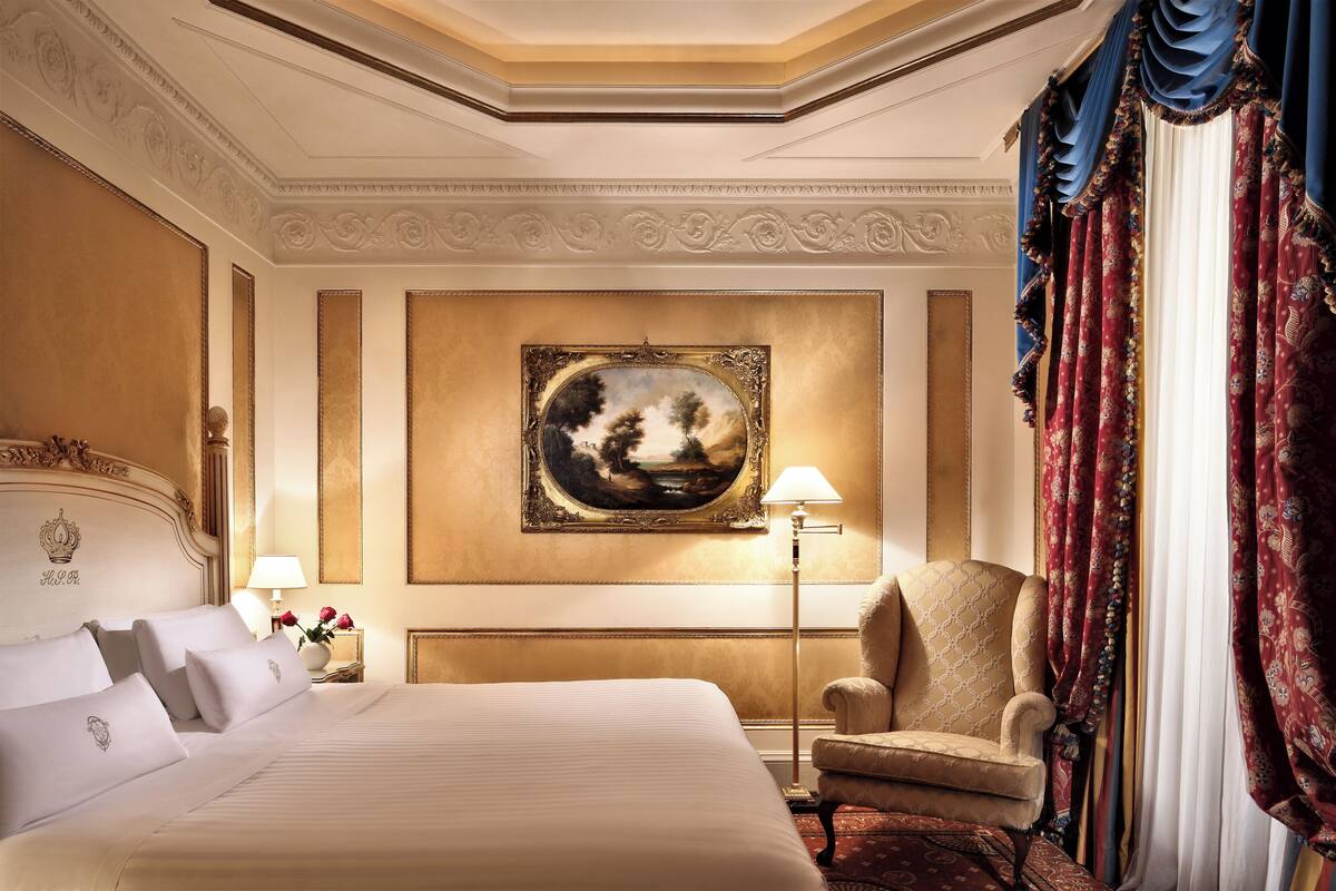Ein Hotelzimmer mit einem großen Bett, einem Sessel, einem Bild an der Wand und einer Lampe.