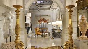 Un lobby imponente con columnas de mármol, una zona de estar central y un espejo decorativo.