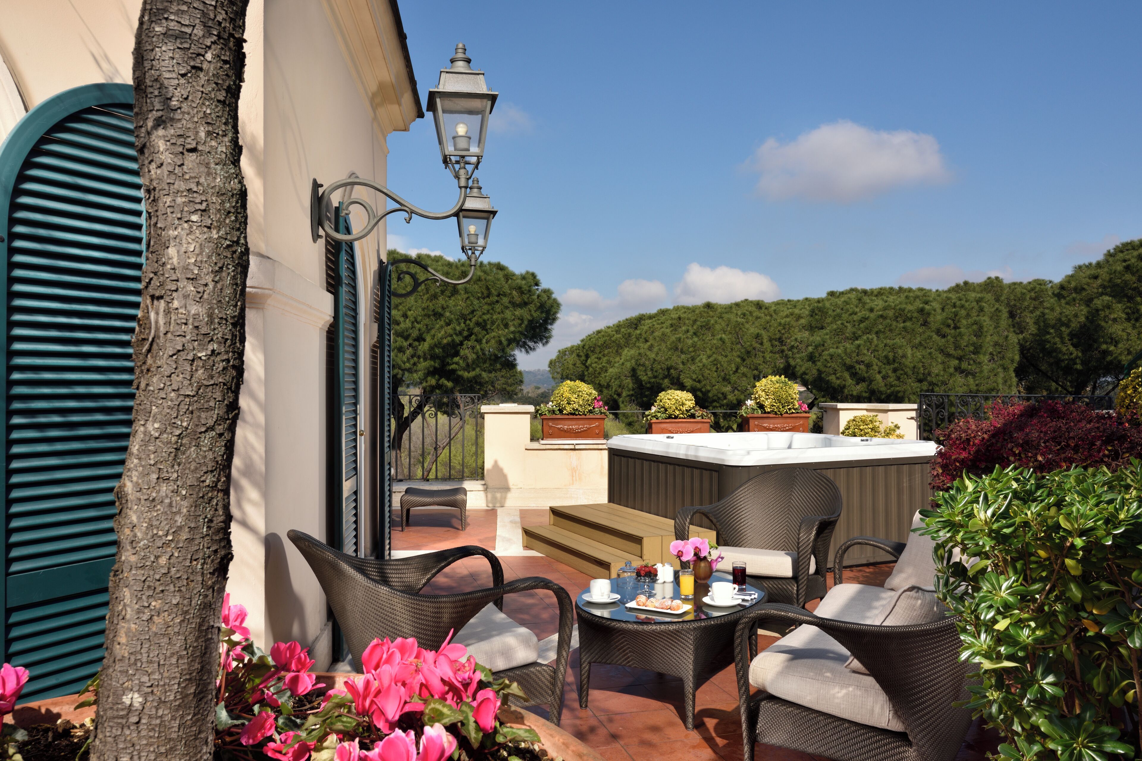 Un espacio al aire libre con muebles de mimbre, una mesa con un jarrón de flores y vistas a una colina boscosa.