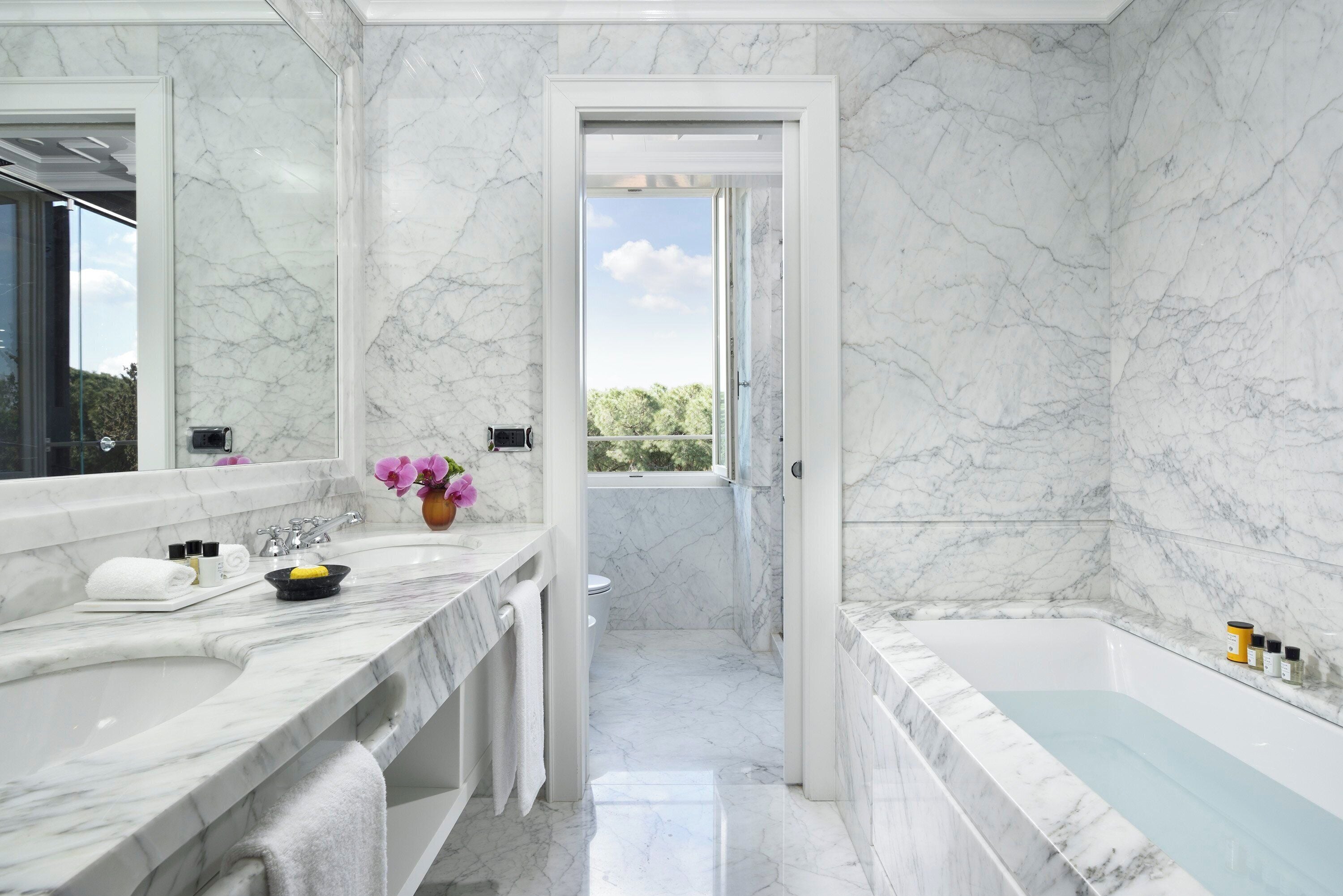 A bathroom with marble walls, a bathtub, and a window leading to a balcony.