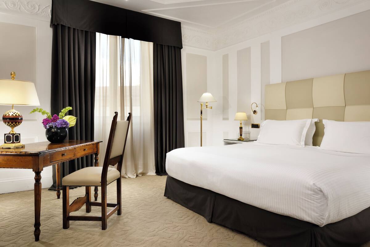 Ein Hotelzimmer mit einem großen Bett, einem Schreibtisch mit Lampe, einem Sessel und einer Blumenvase.