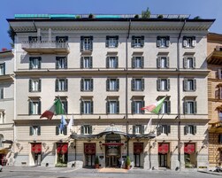 Un hotel a più piani con uno stile architettonico classico, caratterizzato da un ingresso centrale con tenda rossa e diverse bandiere.
