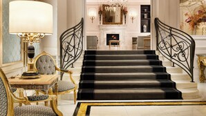 Un magnifique escalier avec des marches noires et des éléments décoratifs dorés, menant à une pièce aux hauts plafonds, illuminée par un lustre.