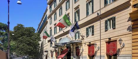 Un hotel con varias banderas, un toldo rojo y un cartel que indica que es un Royal Hotel.