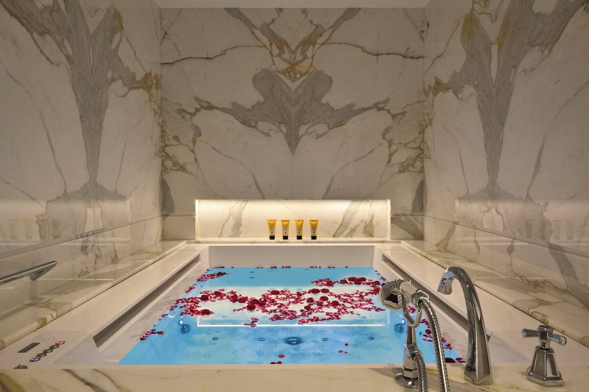 Ein Badezimmer aus Marmor mit einer Badewanne, Rosenblättern und Pflegeprodukten.