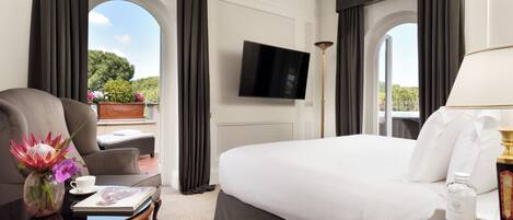 A hotel room with a large bed, a flat-screen TV, a coffee table with a vase of flowers, and a view of the outdoors.
