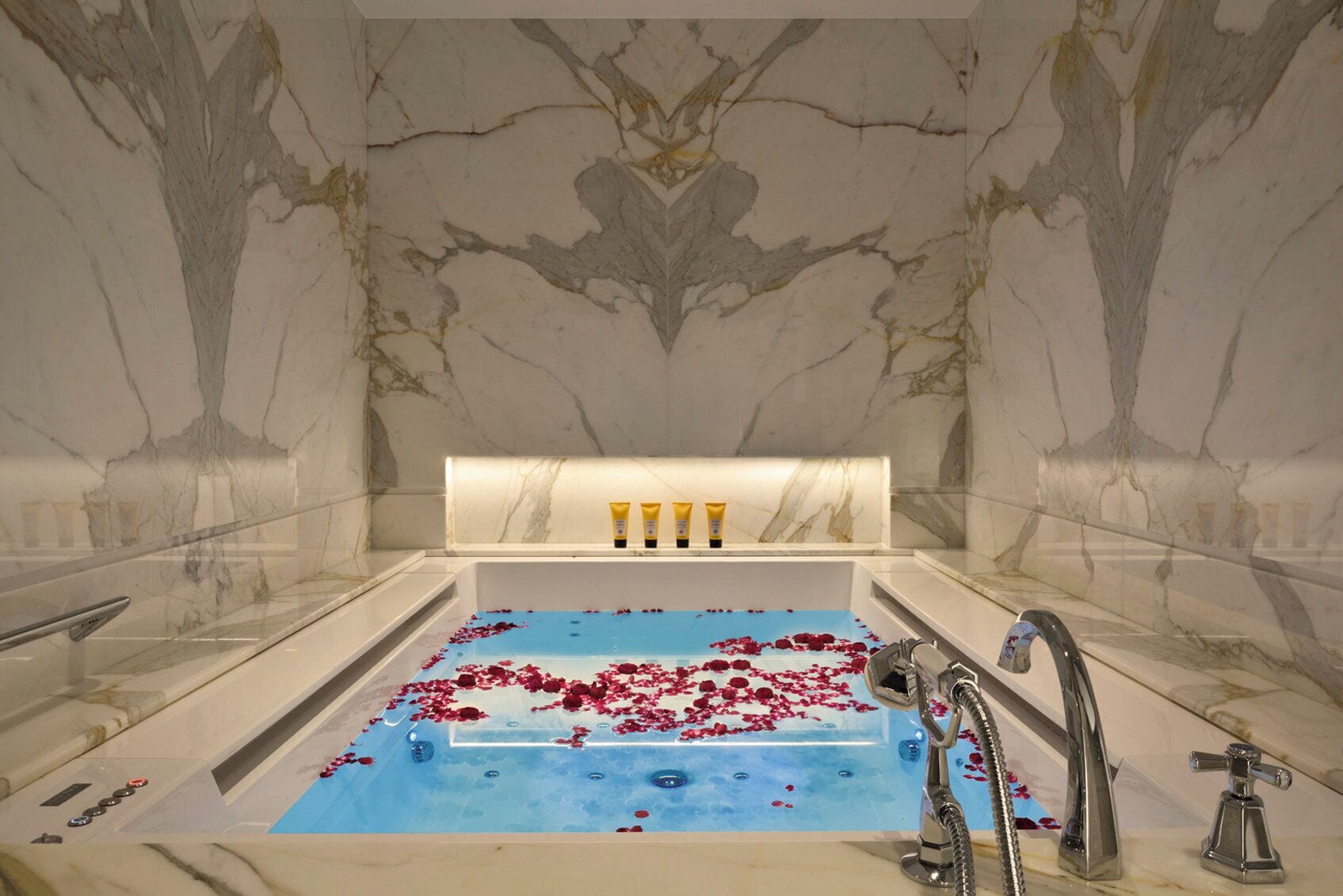 A marble bathroom with a bathtub, rose petals, and toiletries.