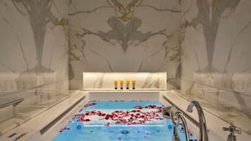 A marble bathroom with a bathtub, rose petals, and toiletries.