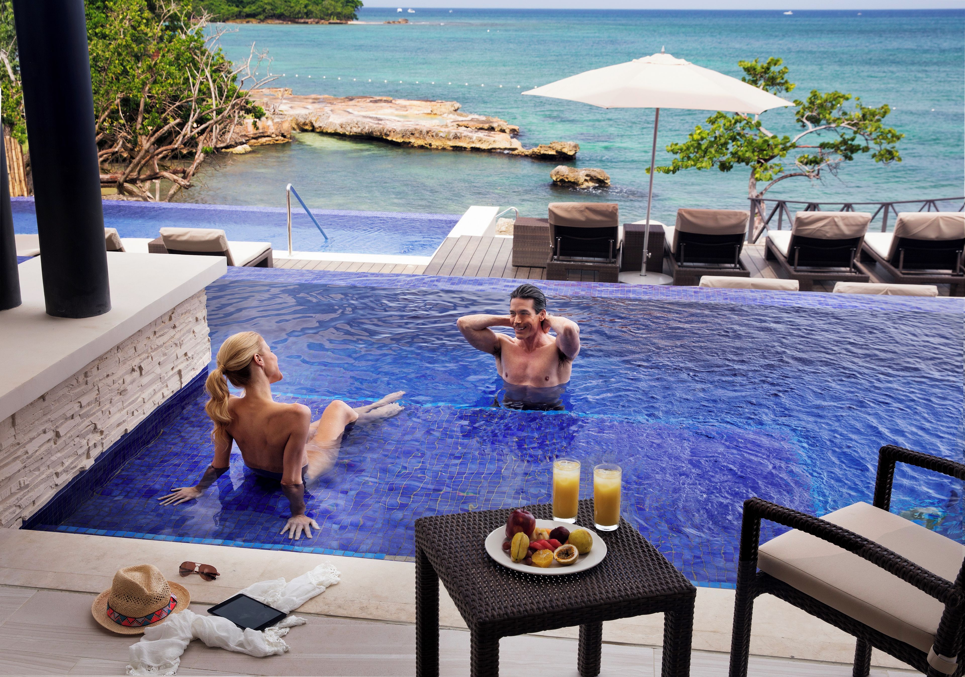 Zona de piscina con vistas al mar, sillas de descanso y una mesa con frutas y bebidas.