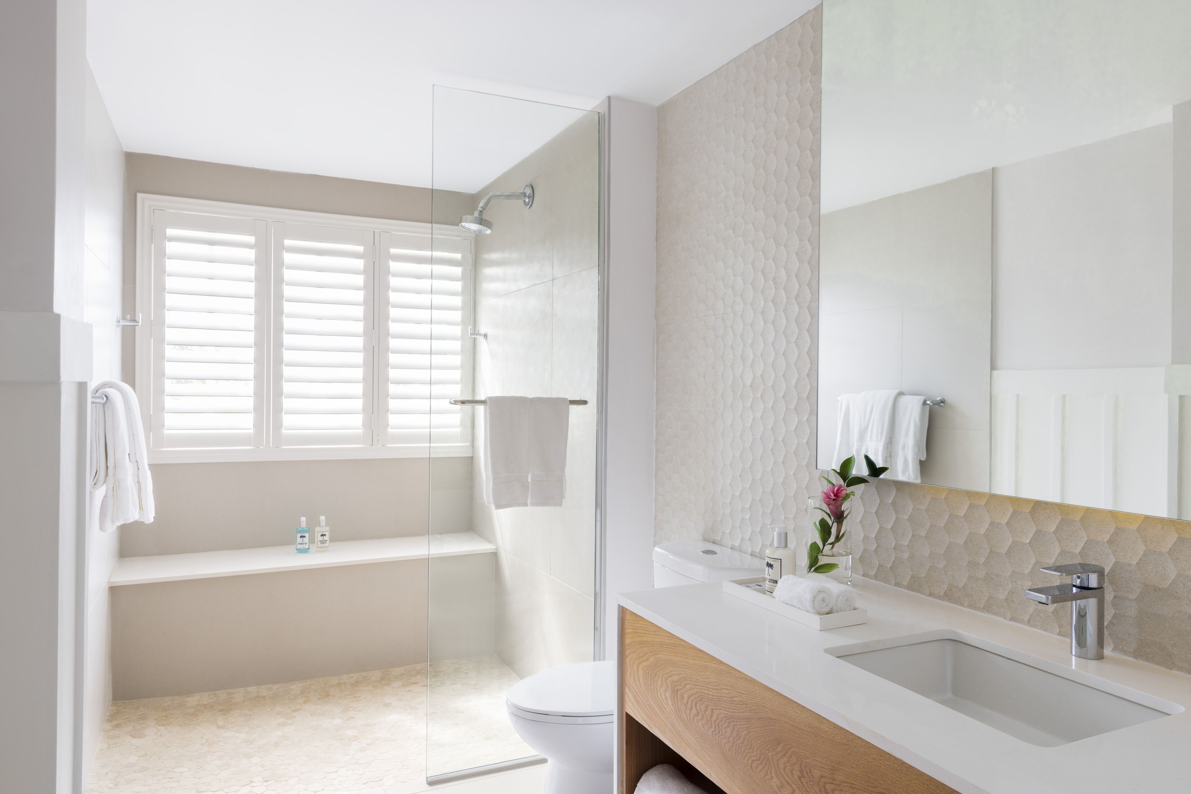 Ein modernes Badezimmer mit einer in Glas abgeschirmten Dusche, einem weißen Waschbecken und einem großen Spiegel.