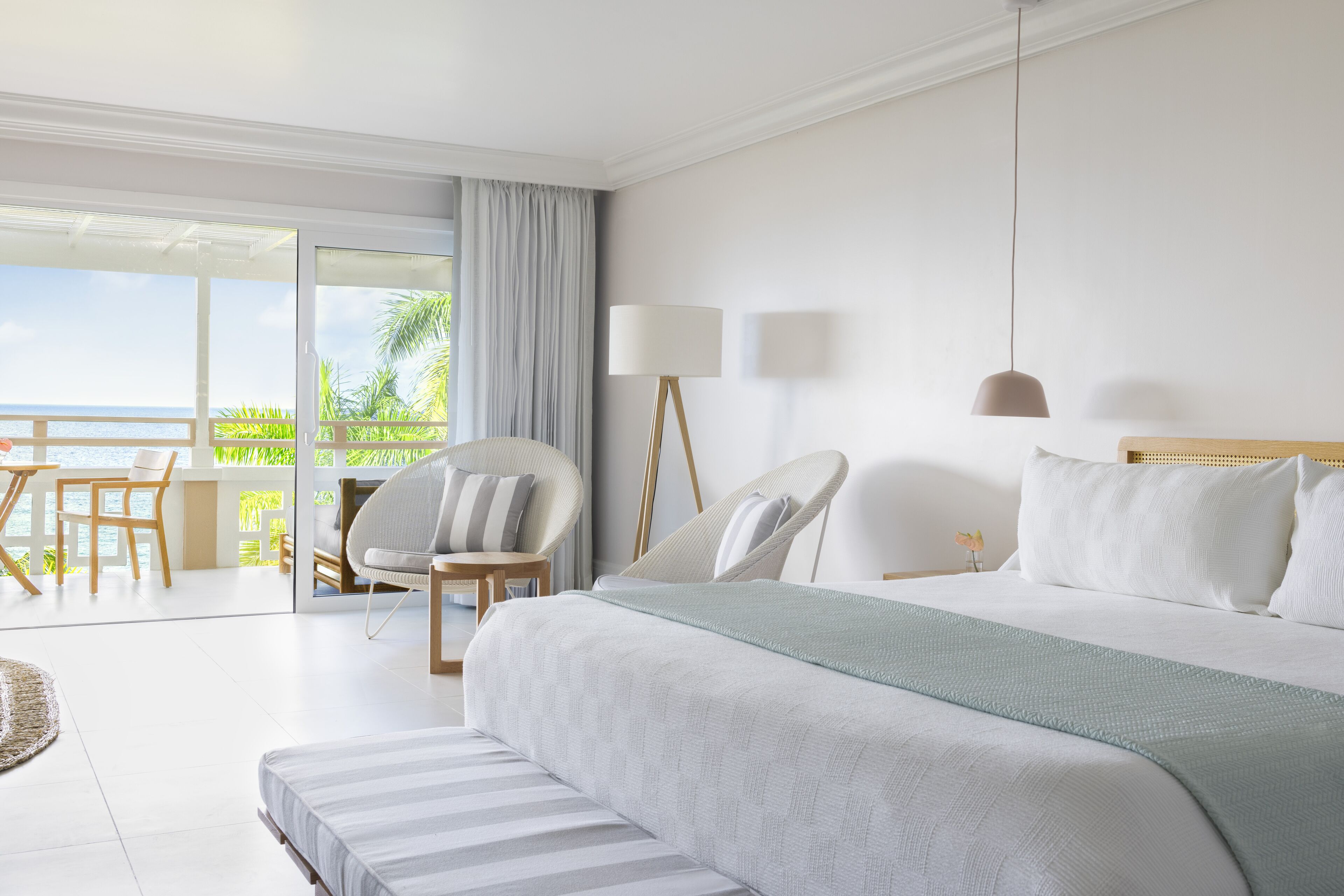Habitación de hotel con una cama grande, un balcón con vistas al mar y una zona de estar con sillas y una mesa.