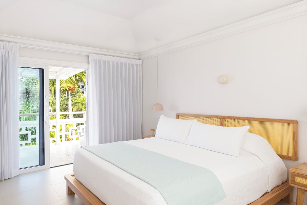 A bedroom with a bed, a nightstand, a lamp, and a view through a glass door to an outdoor area.